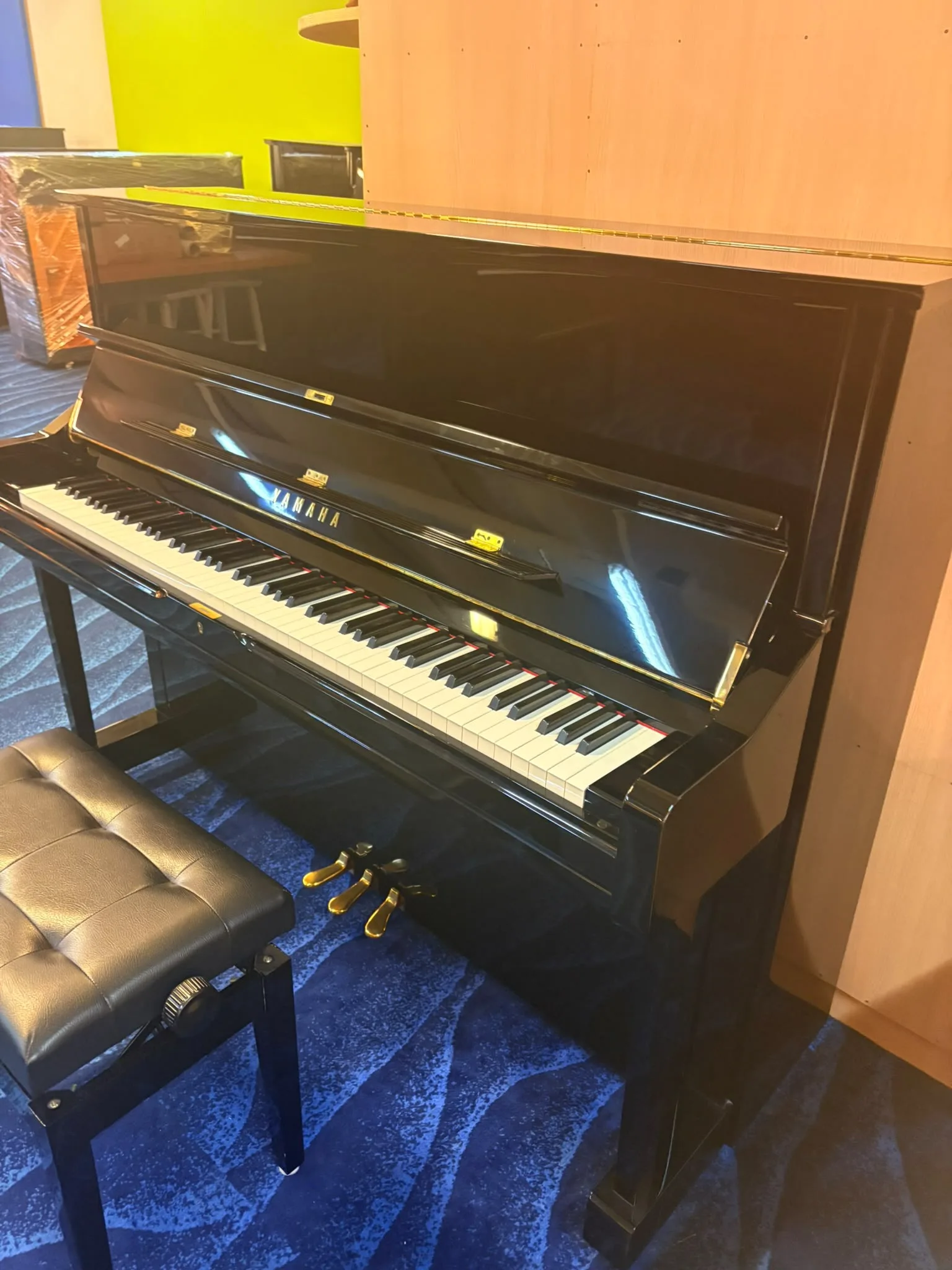 A black Yamaha upright piano with a leather bench in the viewing gallery